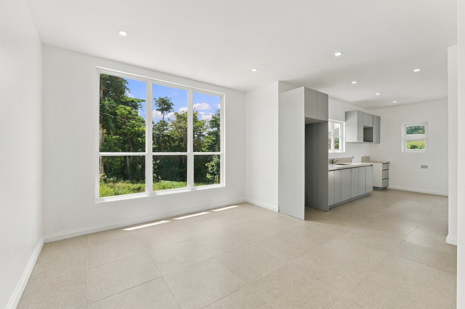 Allspice design, Lot 128: open-plan living area with a large window and grey kitchen beyond.