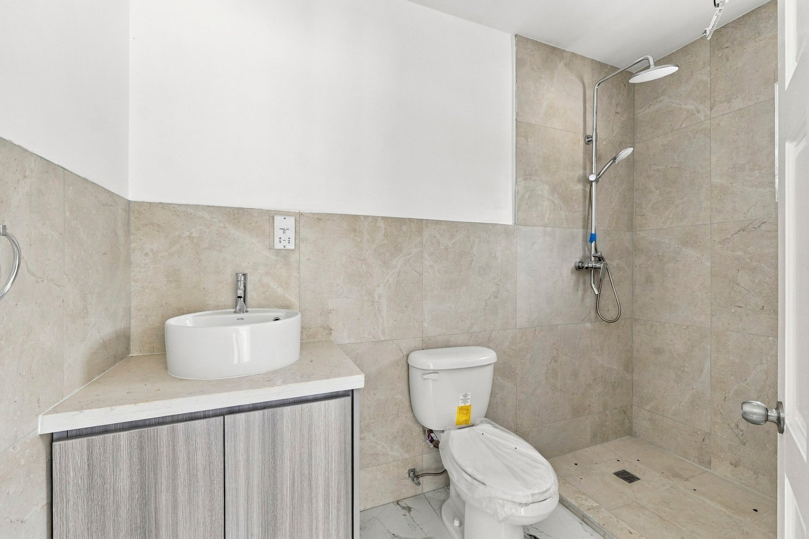 Cinnamon design bathroom with a vessel basin, toilet, beige tiled walls and an open shower area.
