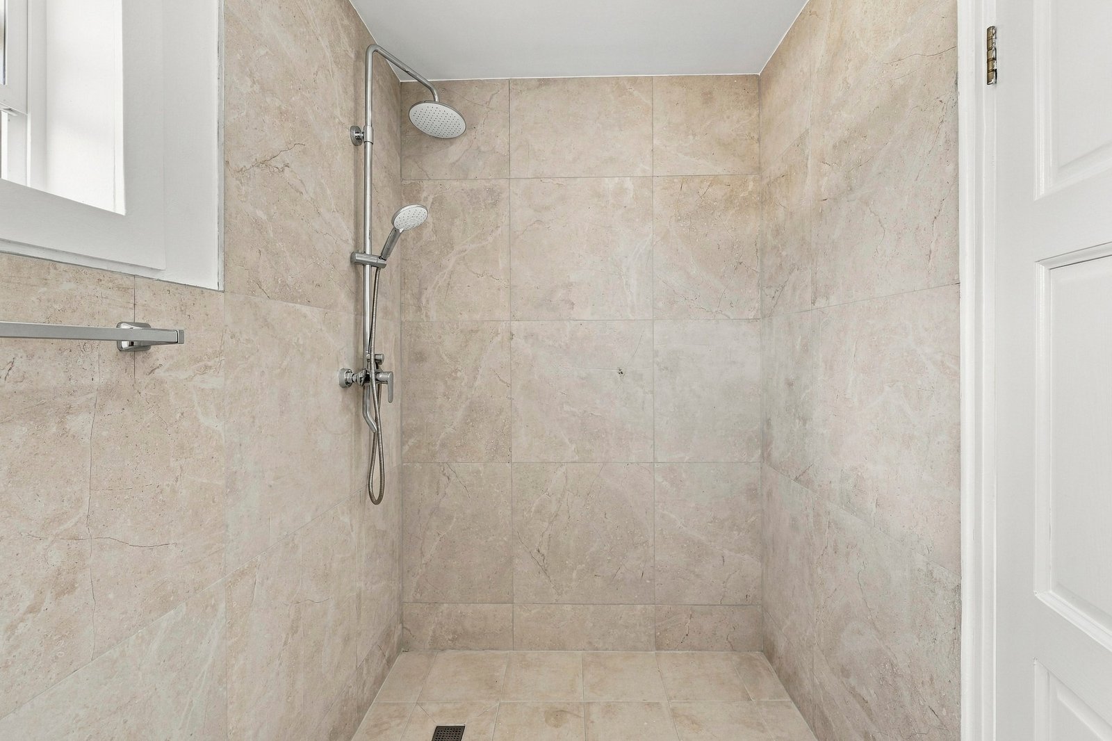 Cinnamon design shower area with beige wall tiles, overhead and handheld shower fittings and a floor drain.
