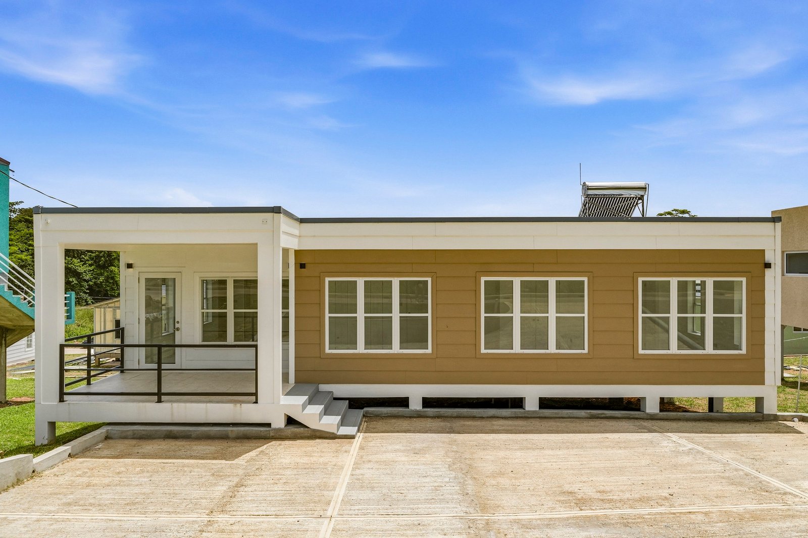 Front exterior of Cinnamon Lot 117, with mustard-coloured cladding, white trim, a railed entrance porch and a paved forecourt.