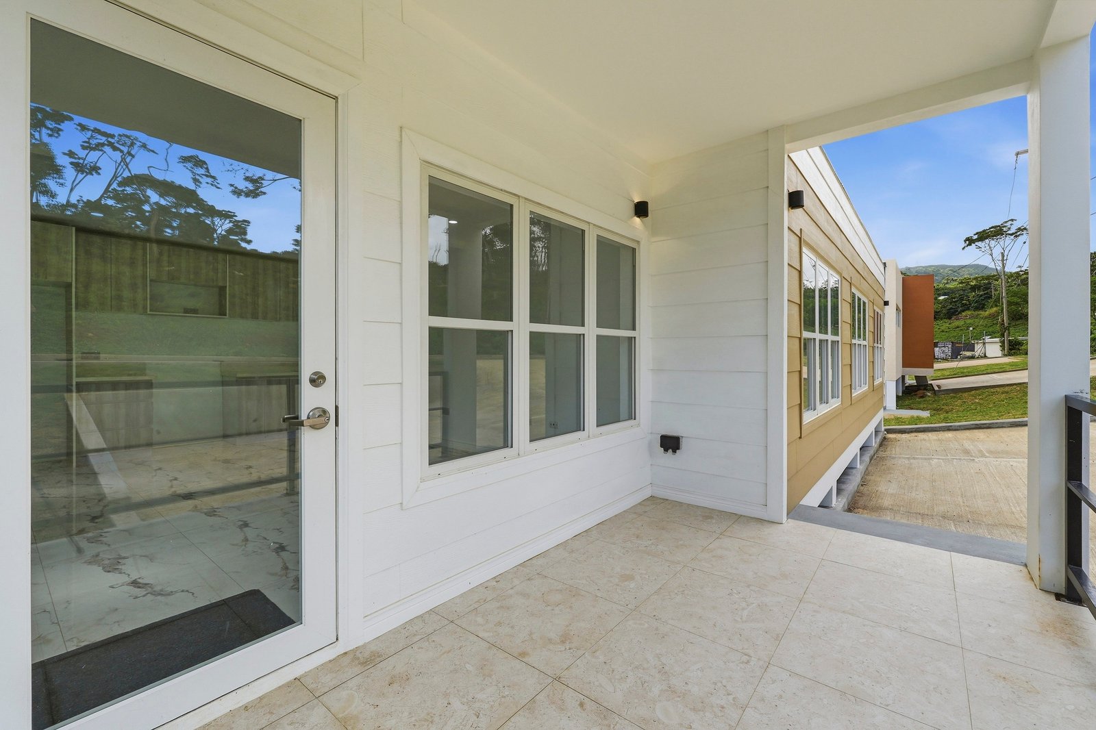 Cinnamon Lot 117 covered porch, with a glazed entrance door, wide window and pale floor tiles.