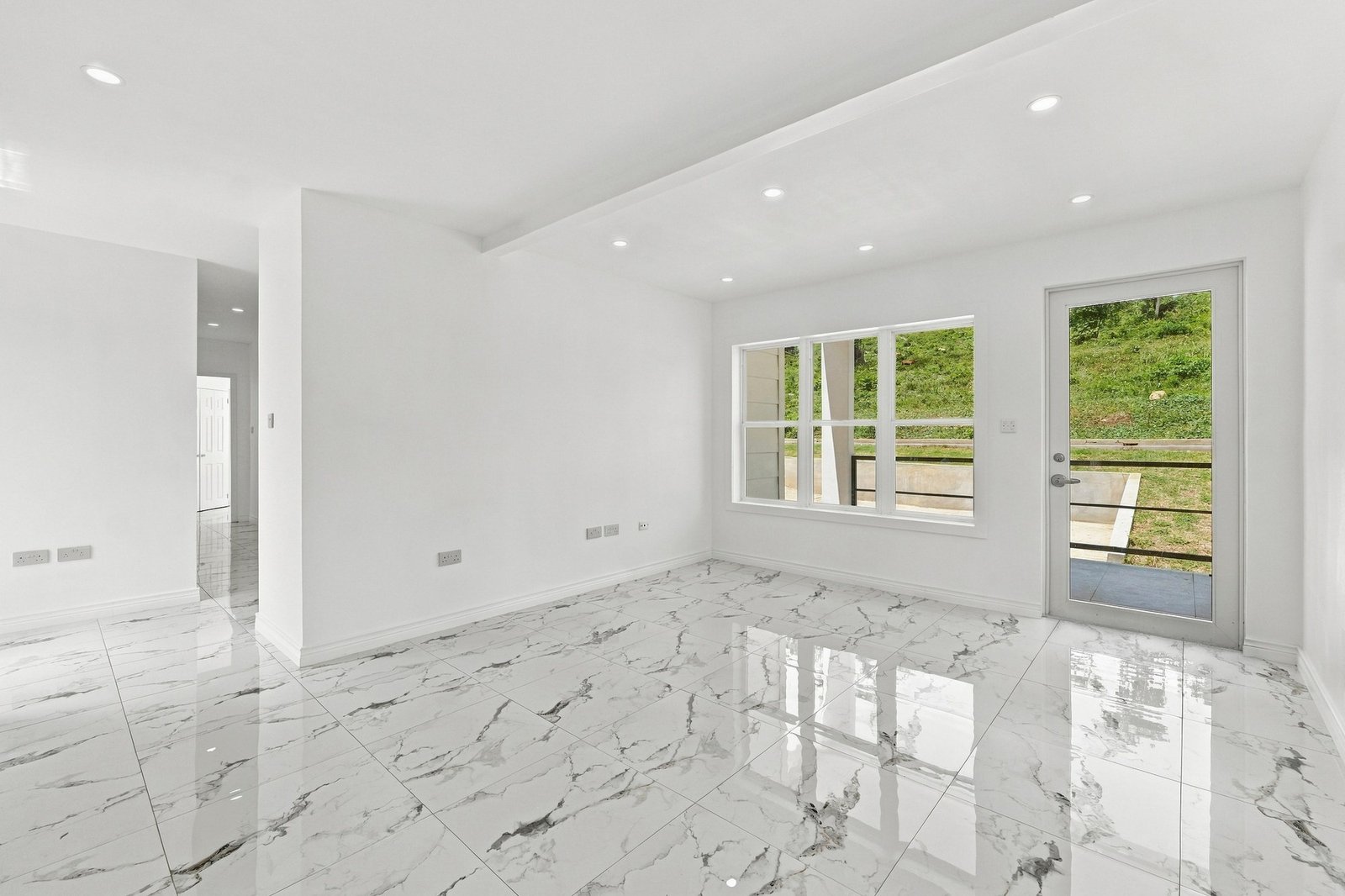 Unfurnished living area at Cinnamon Lot 117, with a glazed entrance door, wide window, recessed lighting and patterned floor tiles.