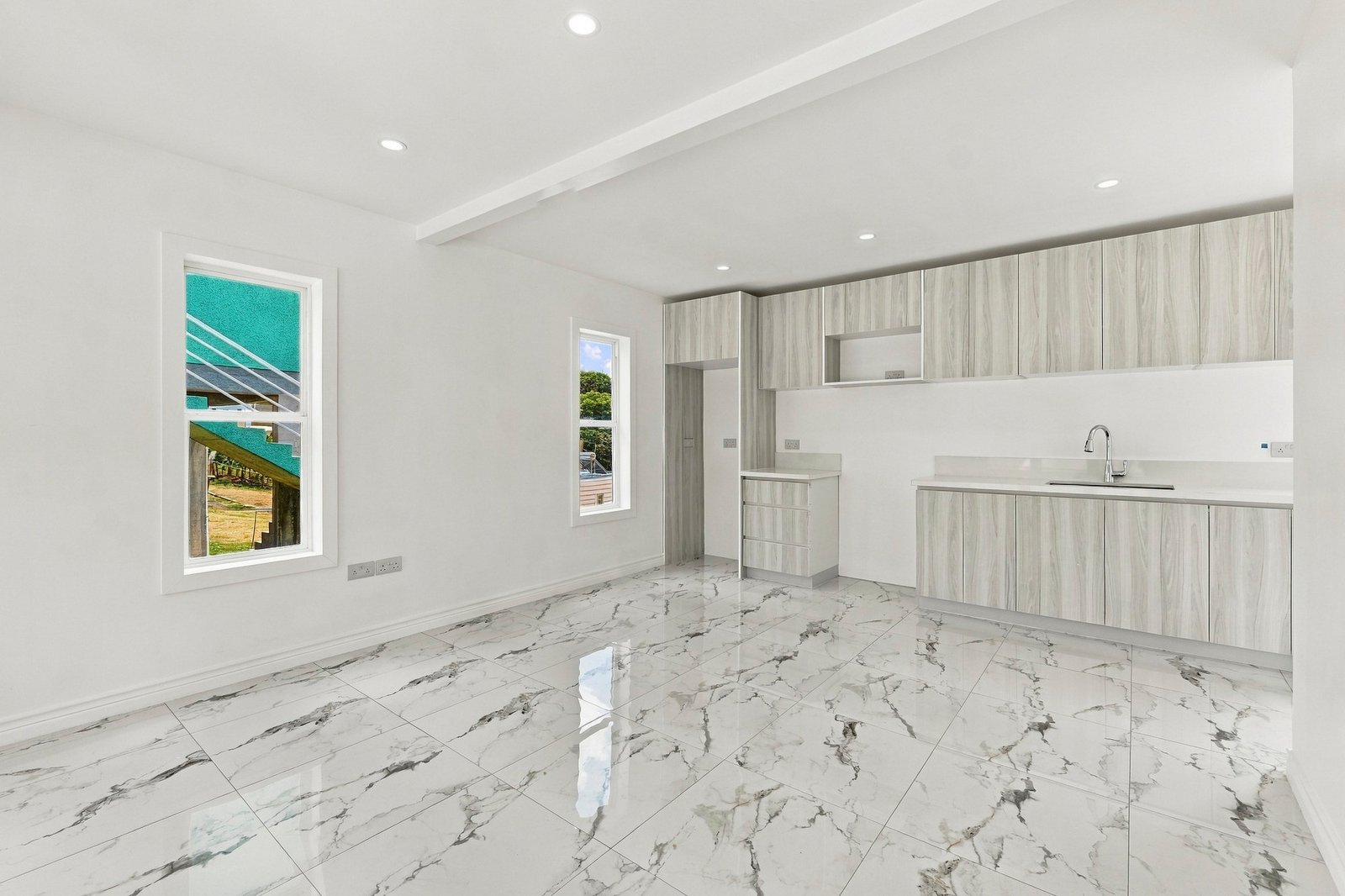 Cinnamon Lot 117 kitchen with pale wood-grain cabinets, a sink, light countertops and white-and-grey patterned floor tiles.