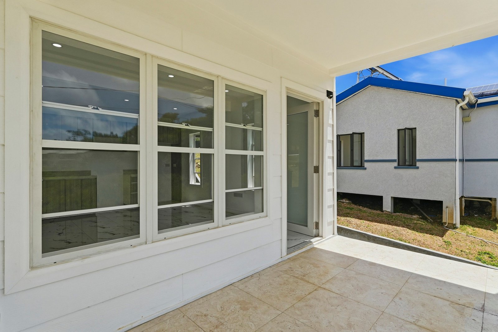 Covered entrance porch at Cinnamon Lot 120, with a glazed door, wide window and pale floor tiles.