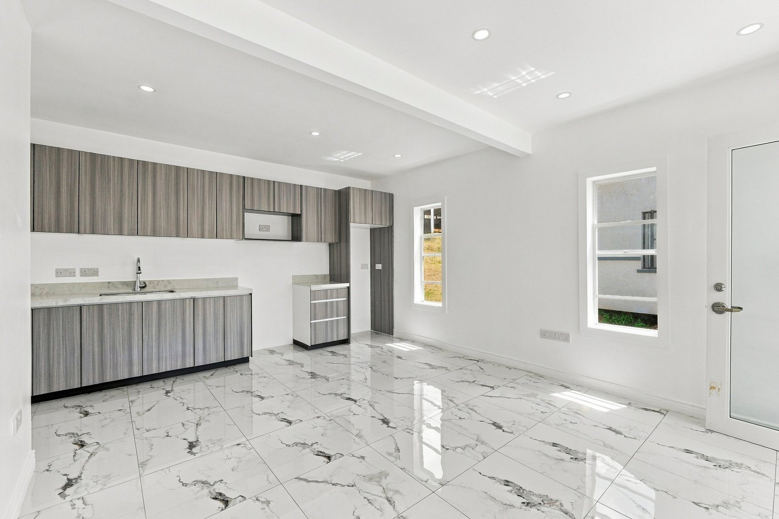 Cinnamon Lot 120 kitchen and open-plan space, with grey wood-grain cabinets, pale countertops and white-and-grey patterned floor tiles.