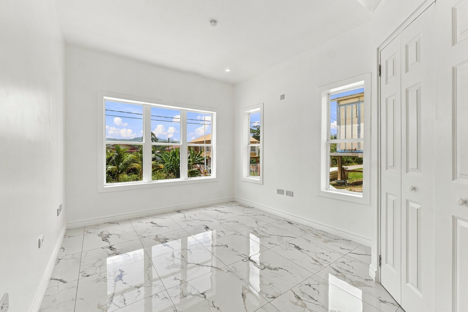 Unfurnished room at Cinnamon Lot 120, with several windows, white cupboard doors and white-and-grey patterned floor tiles.