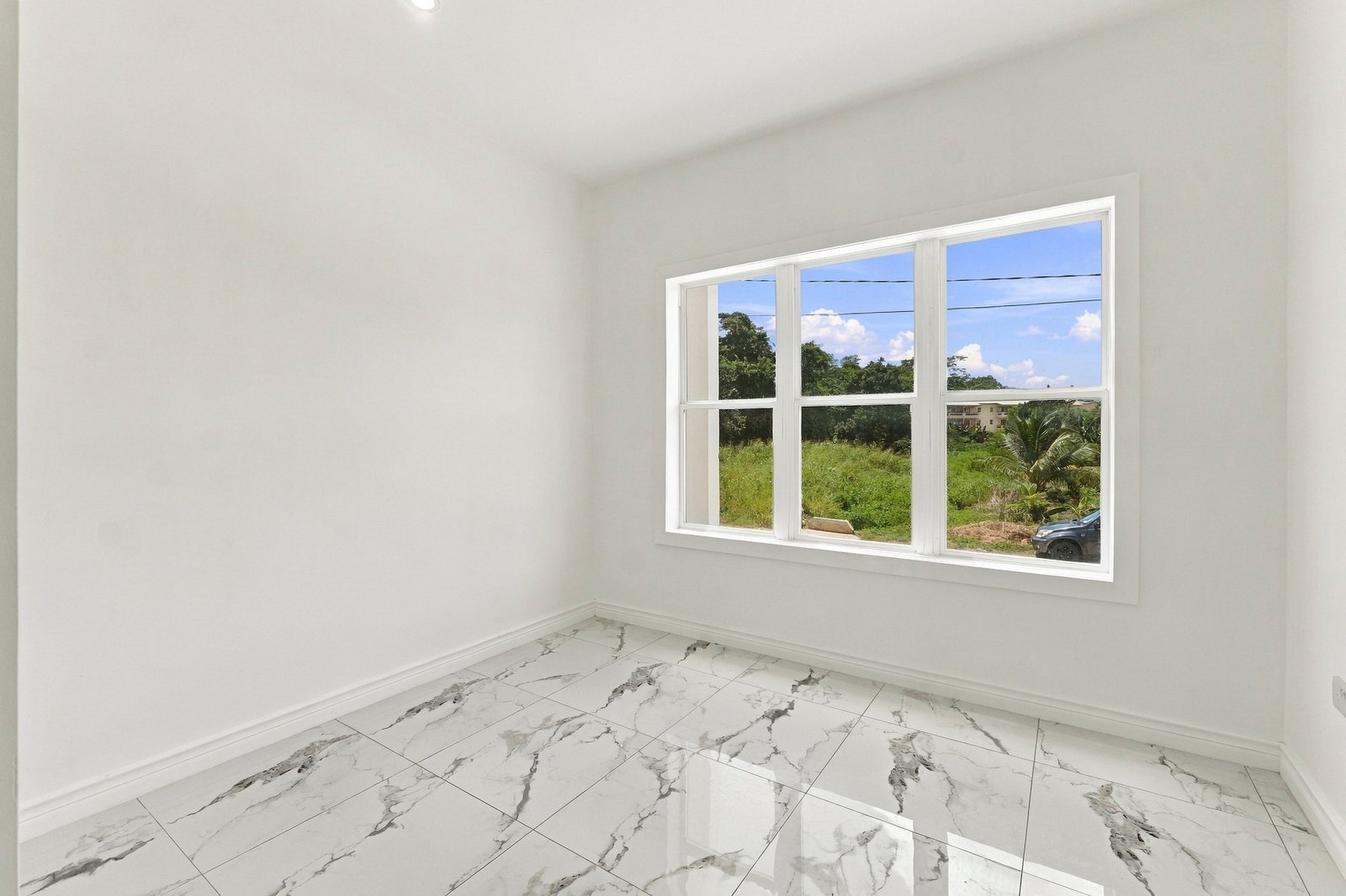 Unfurnished room at Cinnamon Lot 120, with white walls, a wide window overlooking greenery and patterned floor tiles.