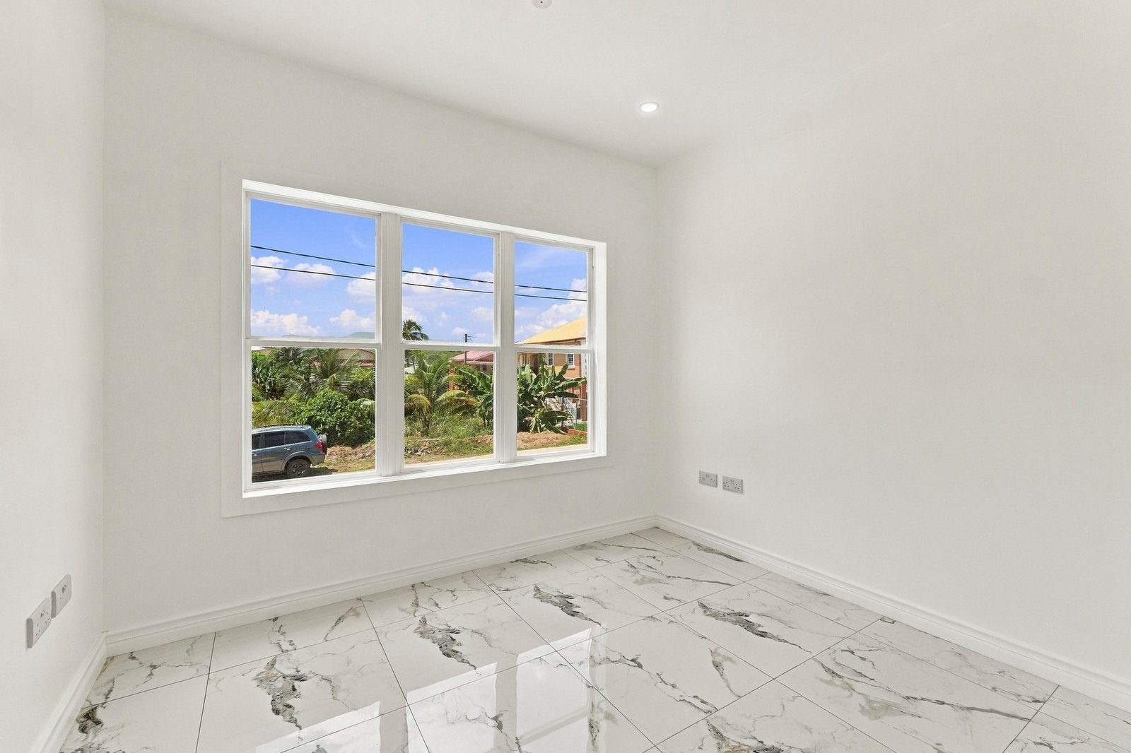 Unfurnished room at Cinnamon Lot 120, with a wide window overlooking the street and white-and-grey patterned floor tiles.