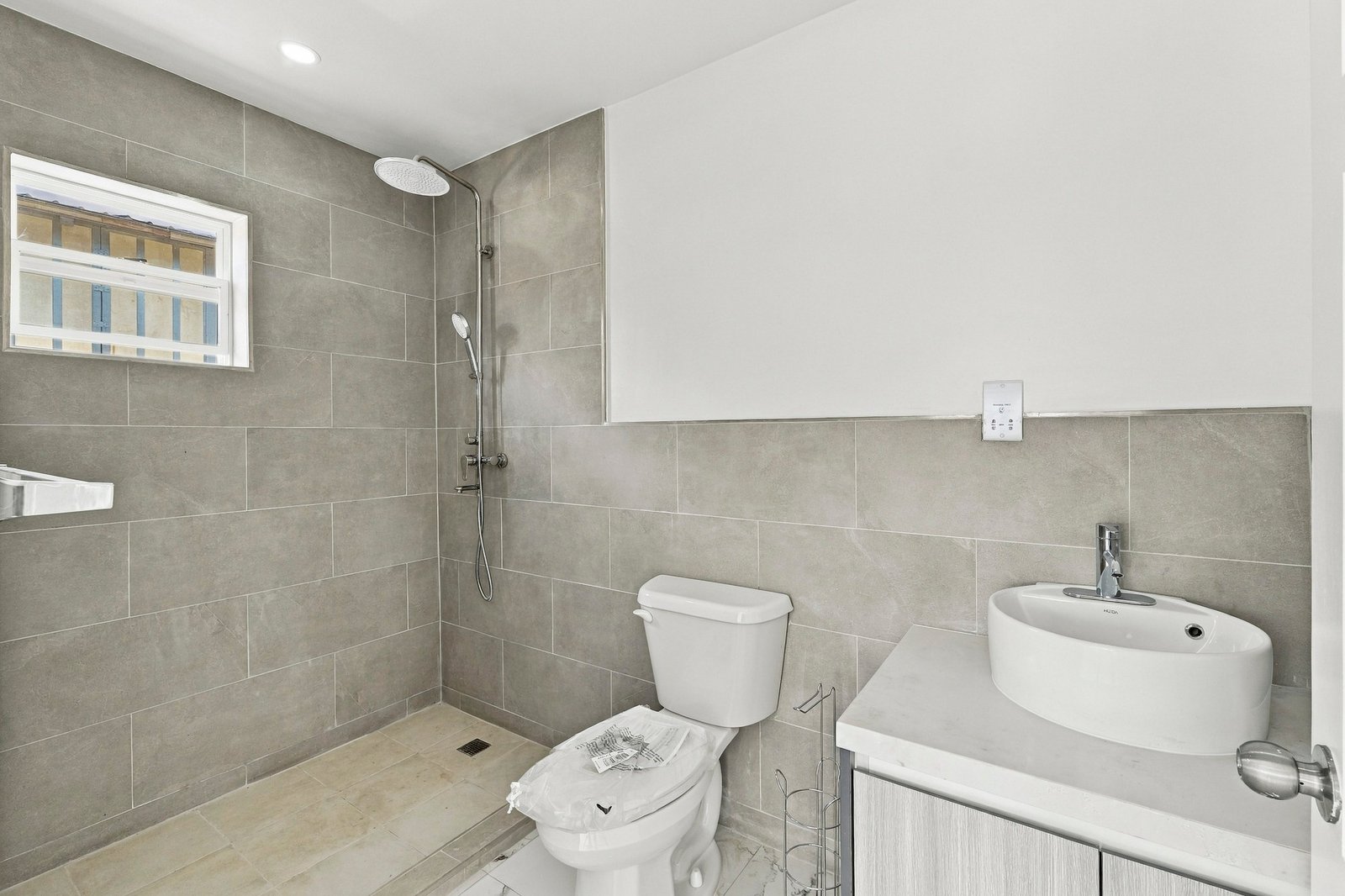 Cinnamon Lot 120 bathroom with grey tiled walls, a vessel basin, toilet and open shower area.