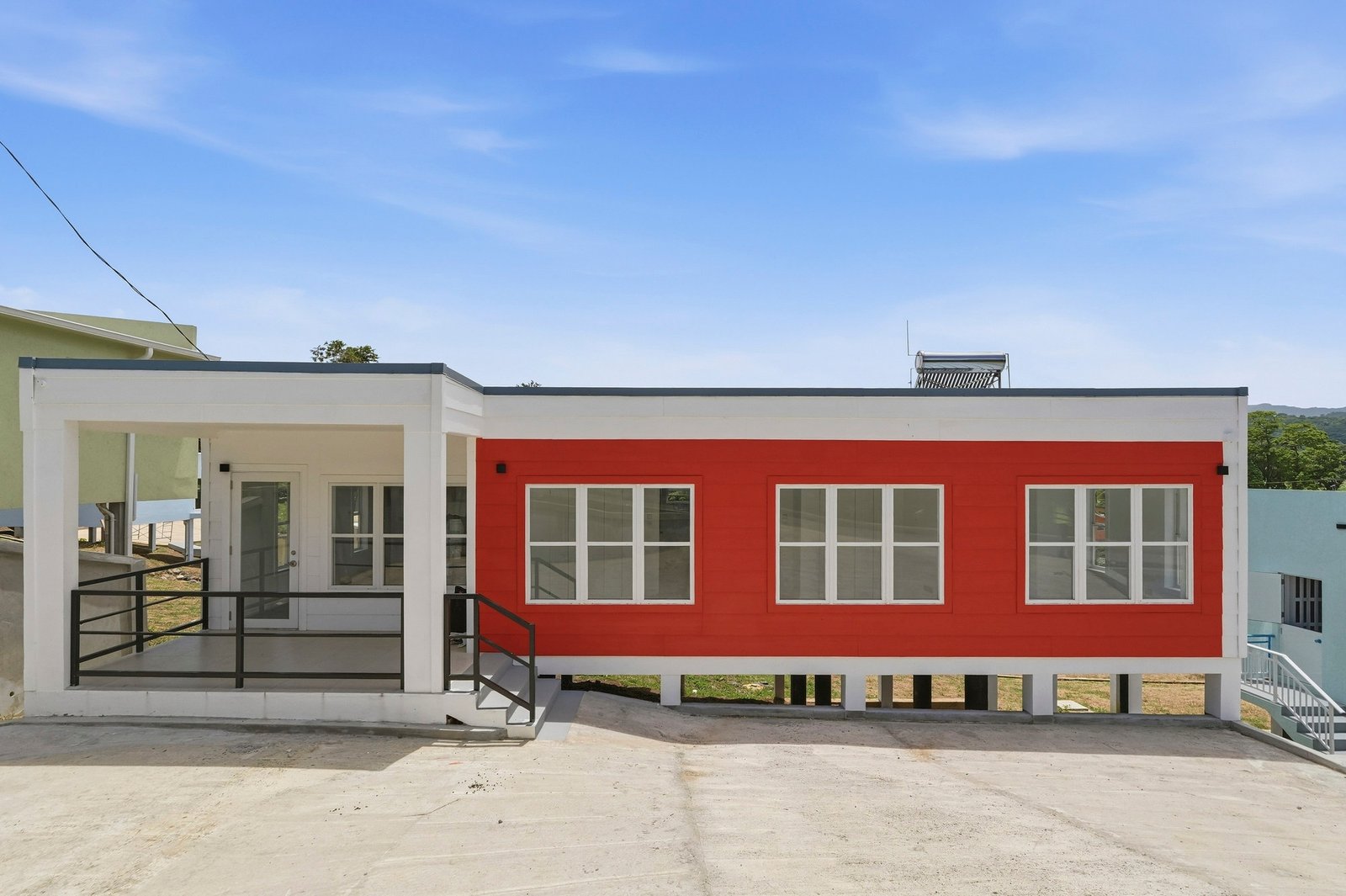 Front exterior of Cinnamon Lot 125, with a red facade, white trim, a railed covered entrance and a paved forecourt.