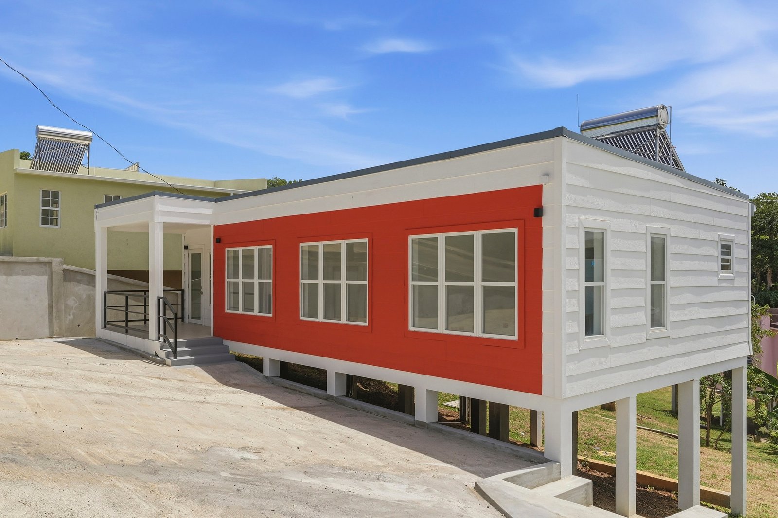 Angled exterior view of Cinnamon Lot 125, showing the red front facade, white side cladding and raised supports on the sloping site.