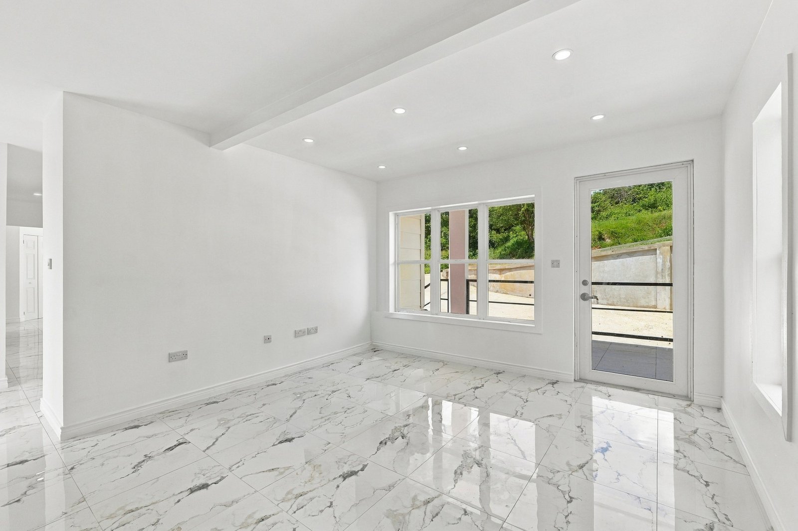 Unfurnished living area at Cinnamon Lot 125, with a glazed entrance door, wide window, recessed lights and patterned floor tiles.