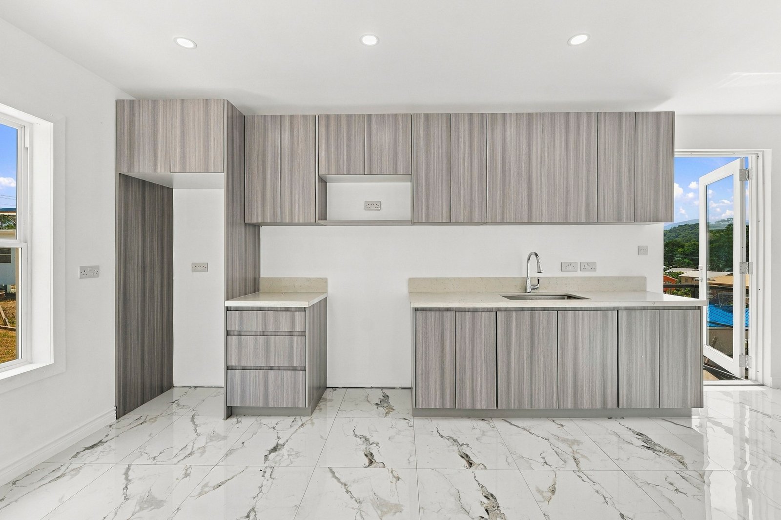 Cinnamon Lot 125 kitchen with grey wood-grain cabinets, a sink and pale countertops.