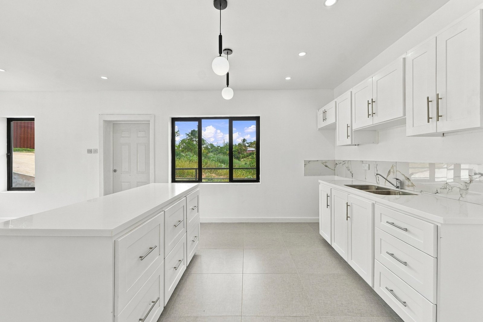 White kitchen in the Clove home on Lot 130, with an island, fitted cabinets, sink and pendant lights.