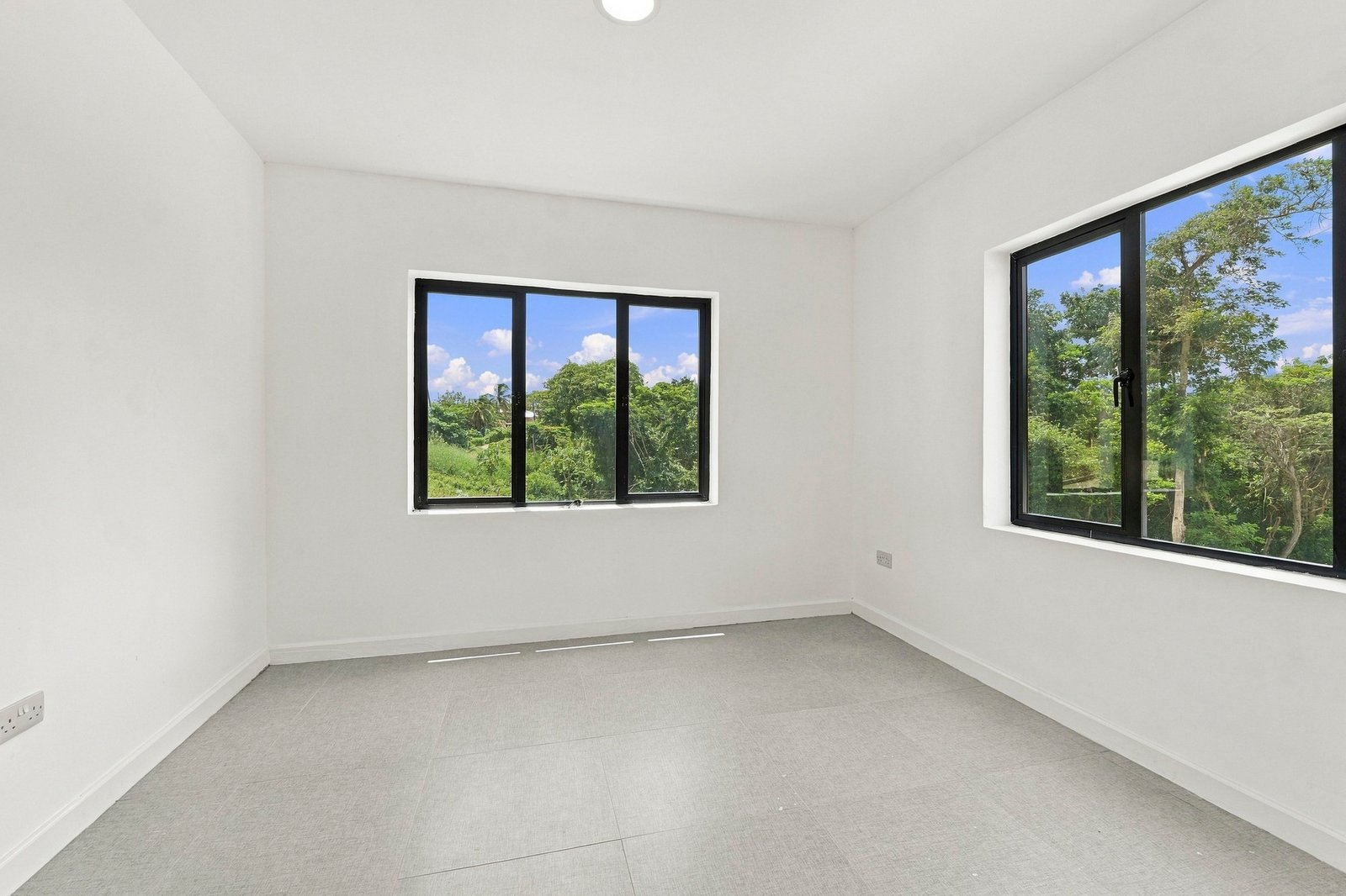 Unfurnished bedroom in the Clove home on Lot 130, with grey floor tiles and windows on two walls.