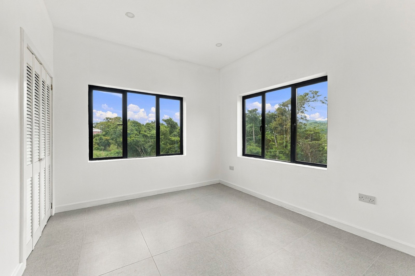 Bedroom in the Clove home on Lot 130, with a louvred closet and two wide black-framed windows.